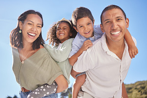 Happy family portrait, parents piggyback children and smile together at outdoor park in blue sky with father. Young couple with cute kids, fun happiness in sunshine and beautiful mother with child, a Photo by Peopleimages.com