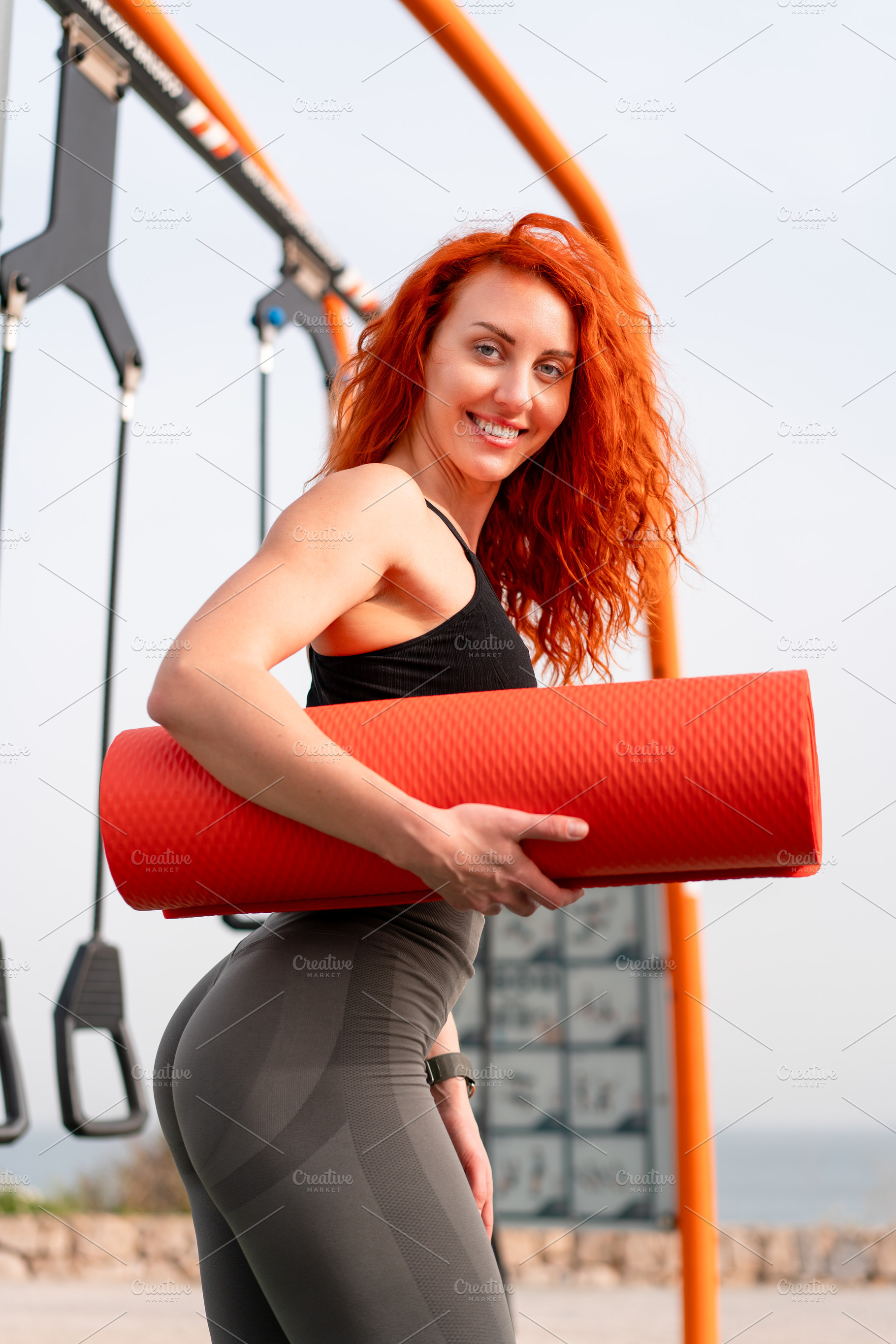 Happy jogger woman holding rolled up exercise mat at outdoor gym, a Person Photo by andreonegin market