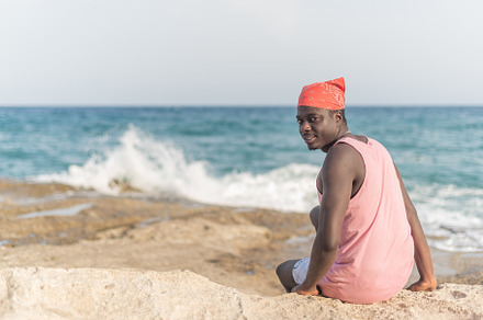 black man sitting on the sand with head turned around, a Holiday Photo by Iván Moreno STOCK PHOTO