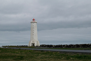 Lighthouse in Akranes, Iceland against a cloudy sky with rocky shoreline, a Photo by AS photostudio