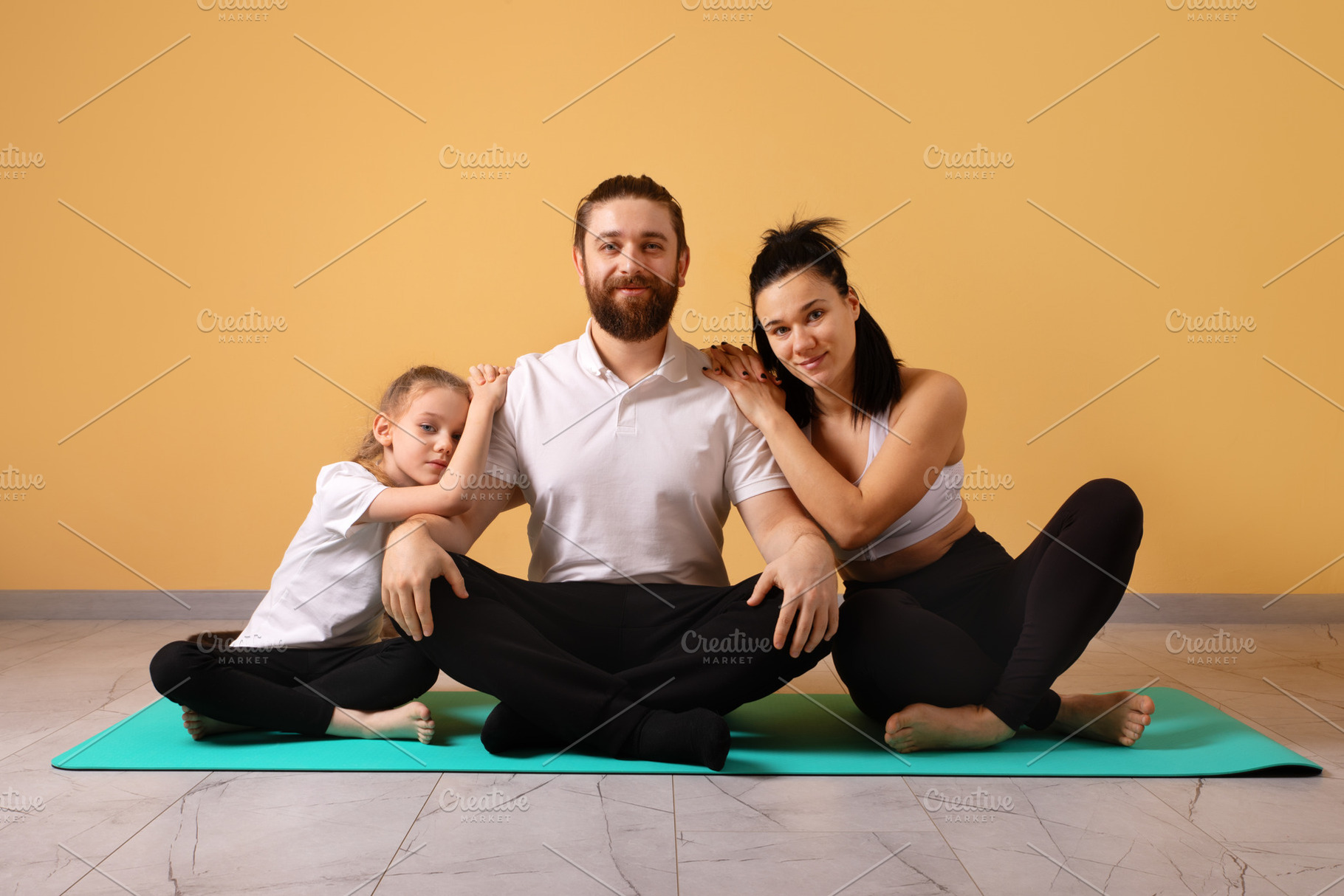 Smiling parents and daughter sit together on a yoga mat at home,, a Person Photo by Ales Munt