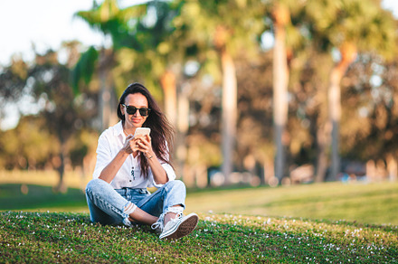 Young woman using mobile phone outdoor in the park, a Person Photo by travnikovstudio