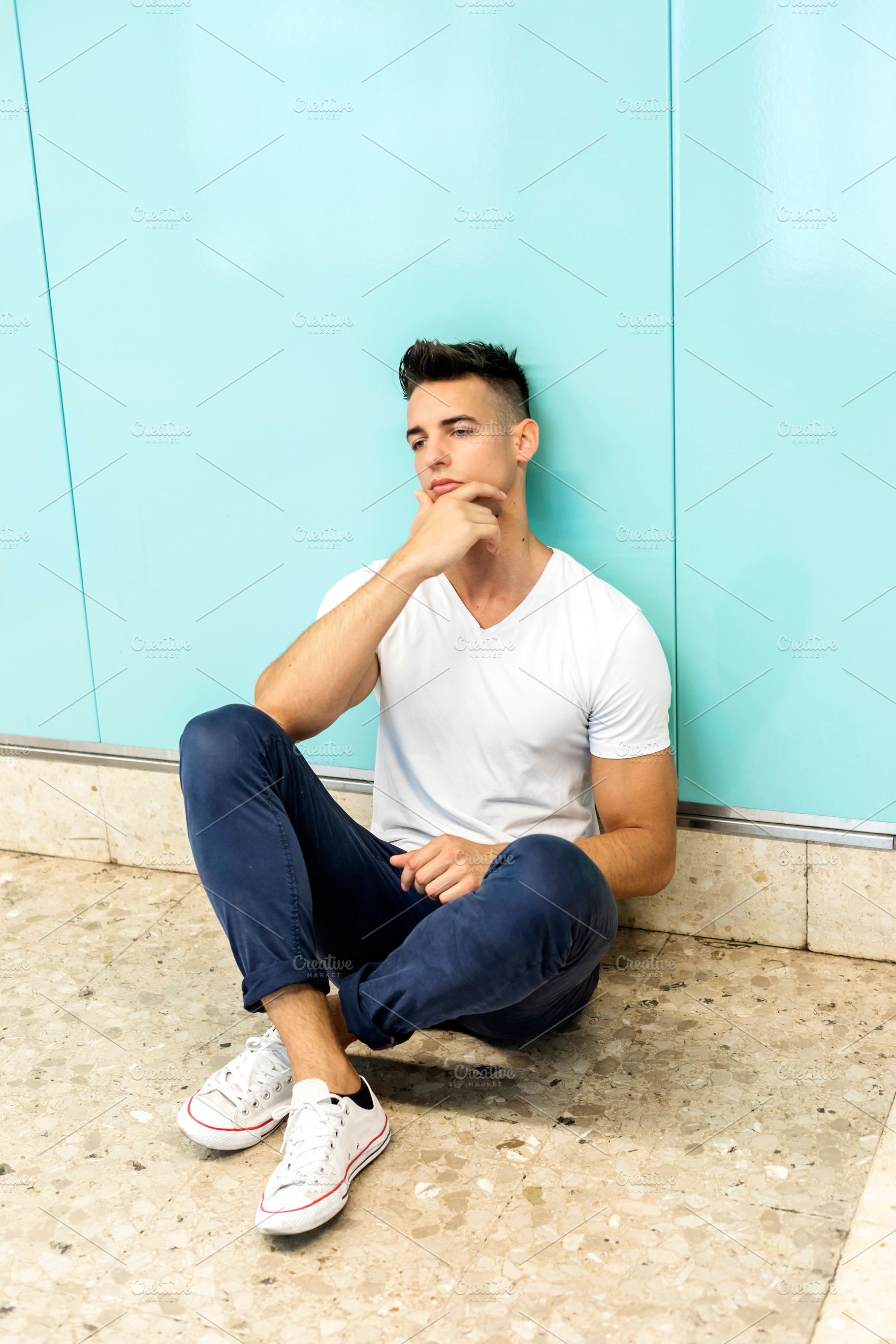 Thoughtful young man sitting against turquoise wall, a Person Photo by RF Images