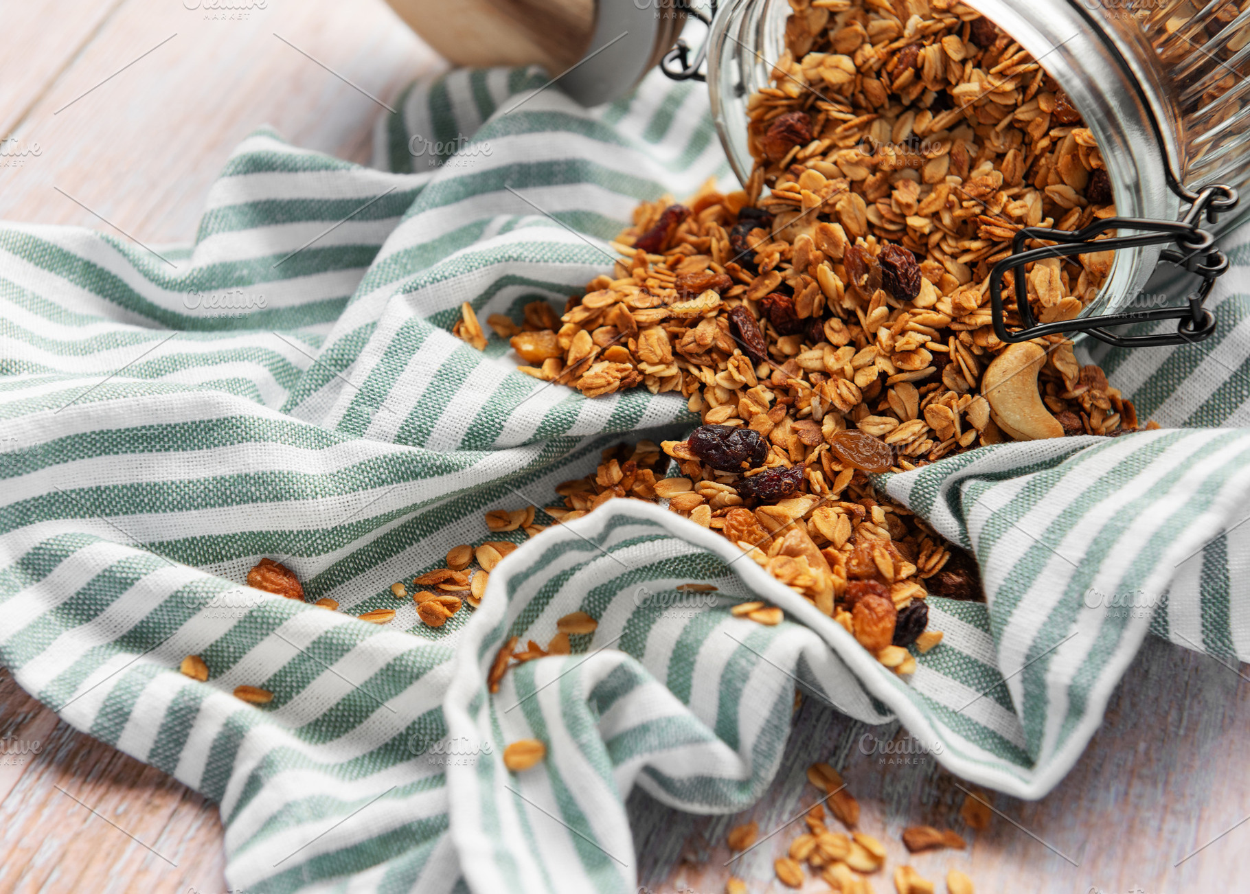 Granola pouring from jar on striped cloth, a Food & Drink Photo by Olena Rudo