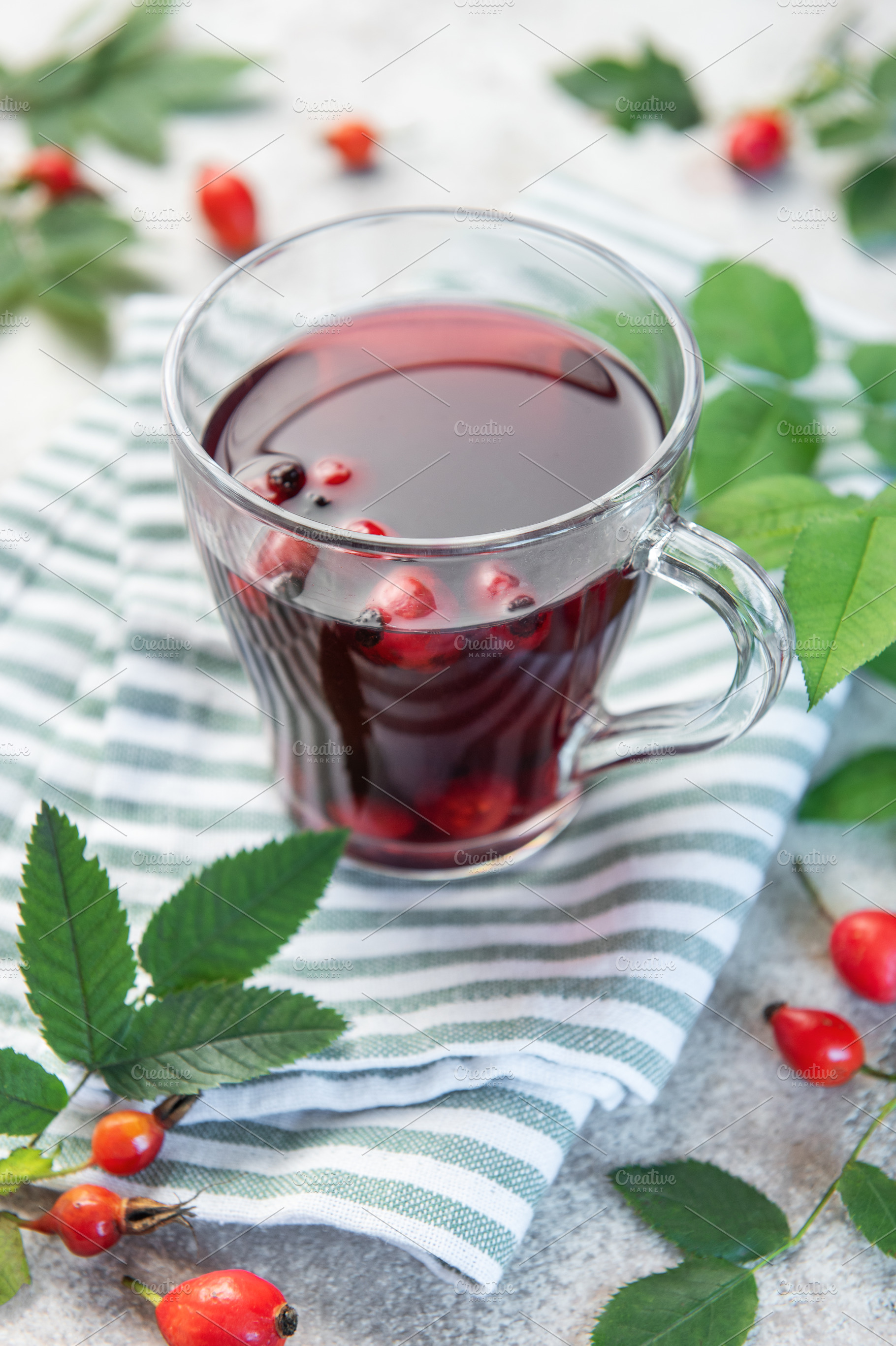 Rosehip tea brewing in glass cup with fresh rose hips and leaves, a Food & Drink Photo by Olena Rudo