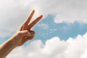 Hand making a peace sign against a bright blue sky, symbolizing, a Photo by salmon.black