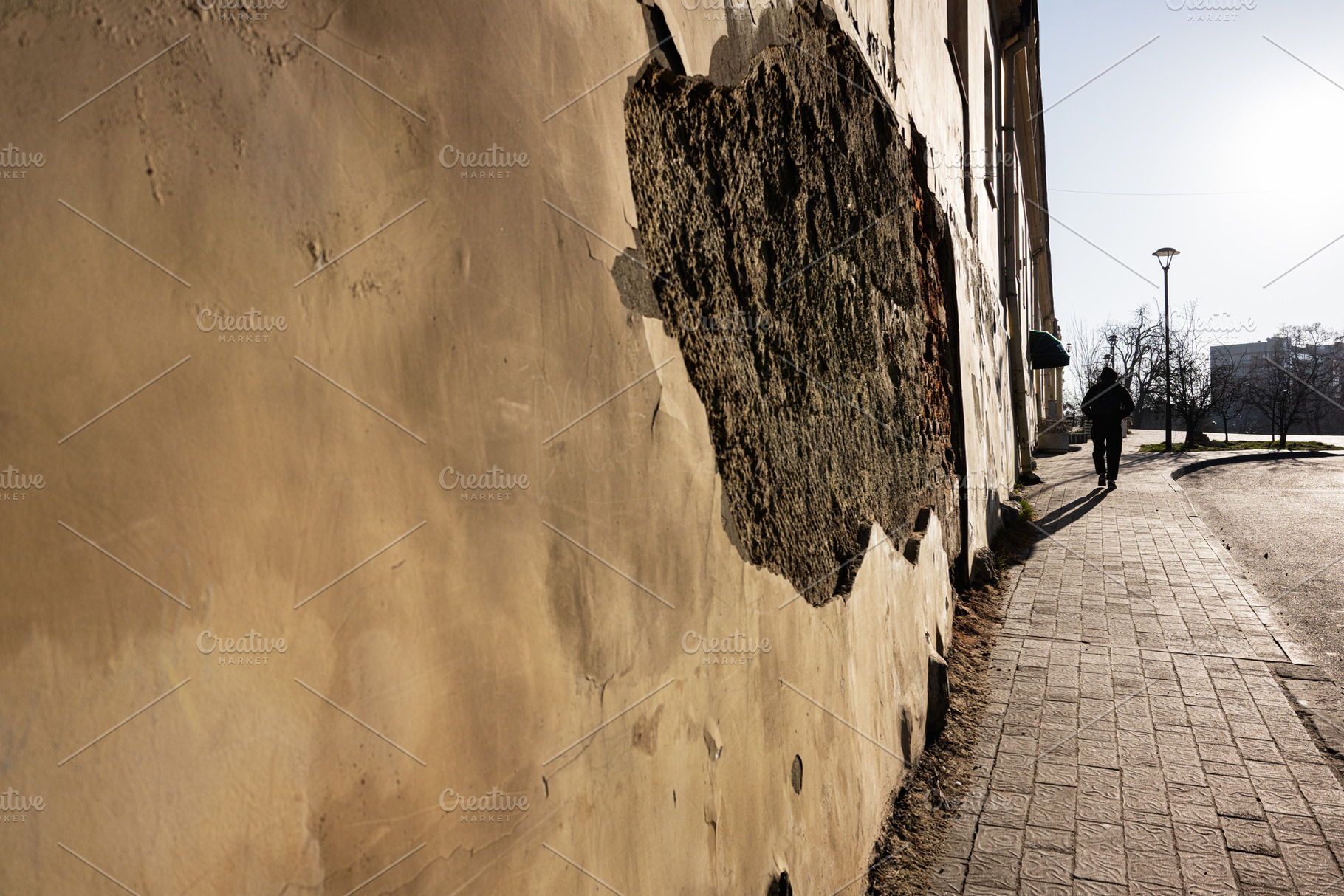 Urban street view with a weathered wall and distant figure walking, a Photo by AS photostudio