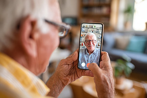 Elderly man using smartphone for video call with family in cozy living room, a Person Photo by AlyaAnd