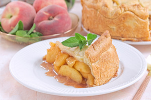 Old fashioned deep dish peach pie slice garnished with fresh mint, on white pla, a Food & Drink Photo by iuliia_n