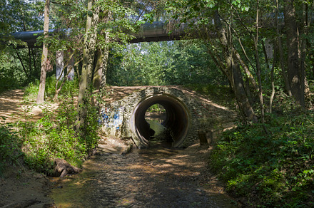 Little river flows in a pipe under the bridge.