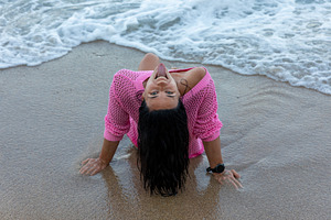 Smiling woman in pink sweater enjoys the beach, leaning back on wet sand with o, a Person Photo by Ales Munt