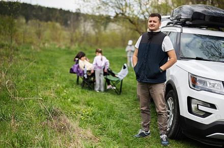 Man in sleeveless vest against suv car with roof rack box, famil, a Person Photo by AS photostudio