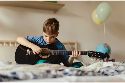 Happy boy playing on the guitar in, a School & Education Photo by HalfPoint