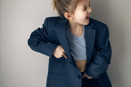 funny portrait of a fashionable girl child in a large gray jacket stands agains, a Person Photo by SaulichPhoto