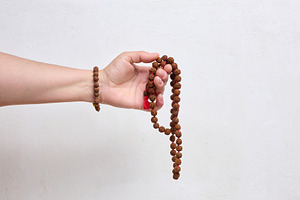 A person holding rudraksha prayer beads in their hand against a
