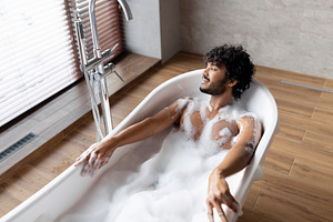 Home spa and relax on weekends. Relaxed indian man lying in bathtub with foam,, a Person Photo by Prostock-Studio