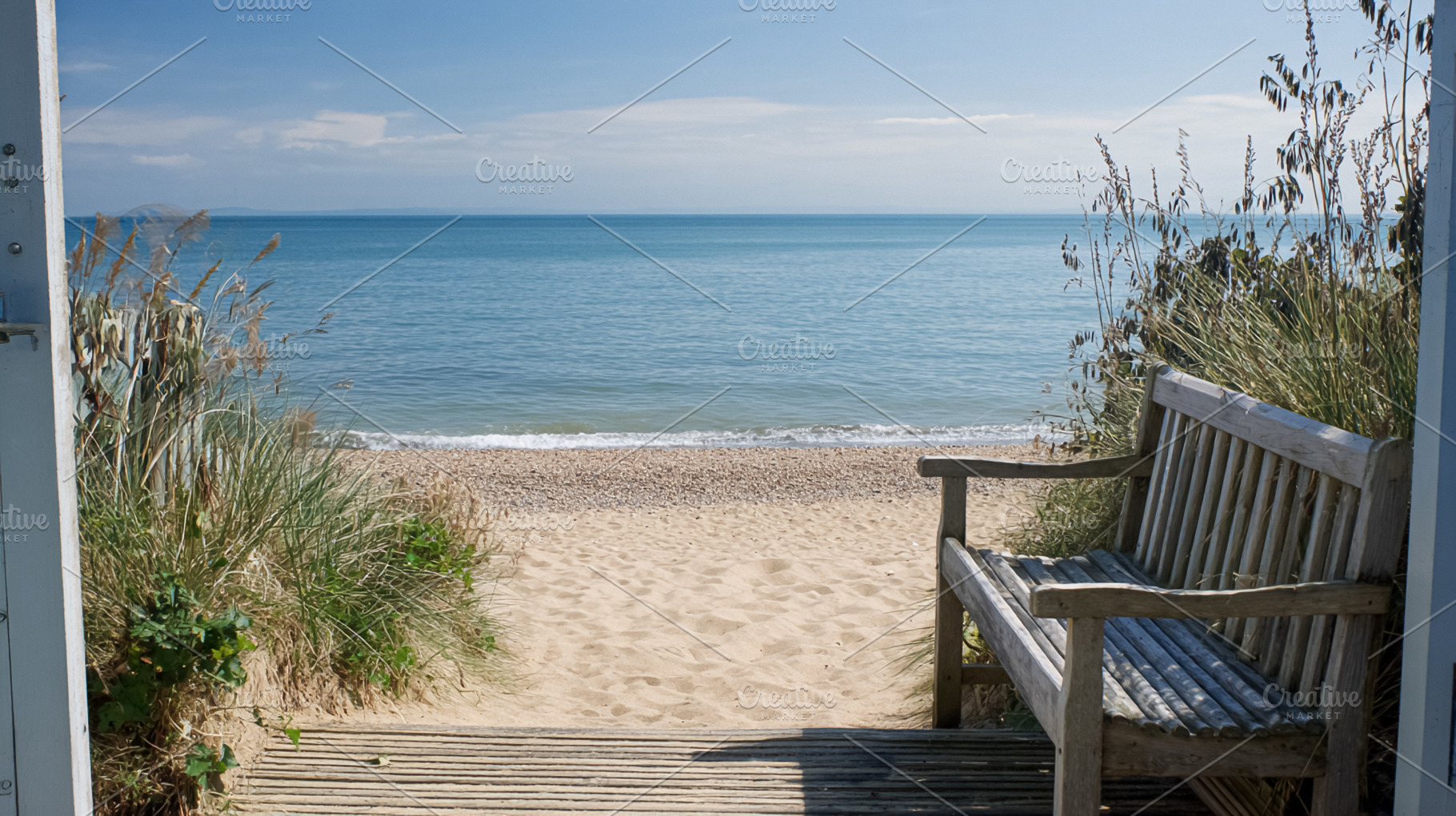 Wooden bench inviting relaxation on a sandy beach leading to the, a Photo by Studio ANNA