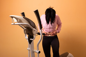 Young woman in sportswear clutching her stomach beside an ellipt, a Person Photo by Ales Munt