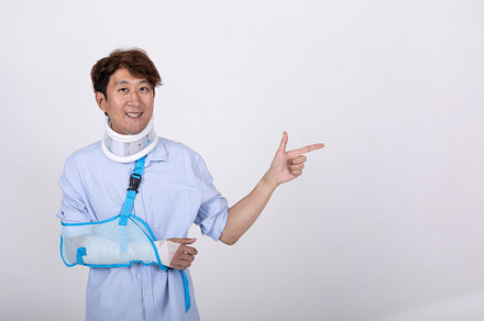Asian man with broken arm and neck pointing finger to empty spac