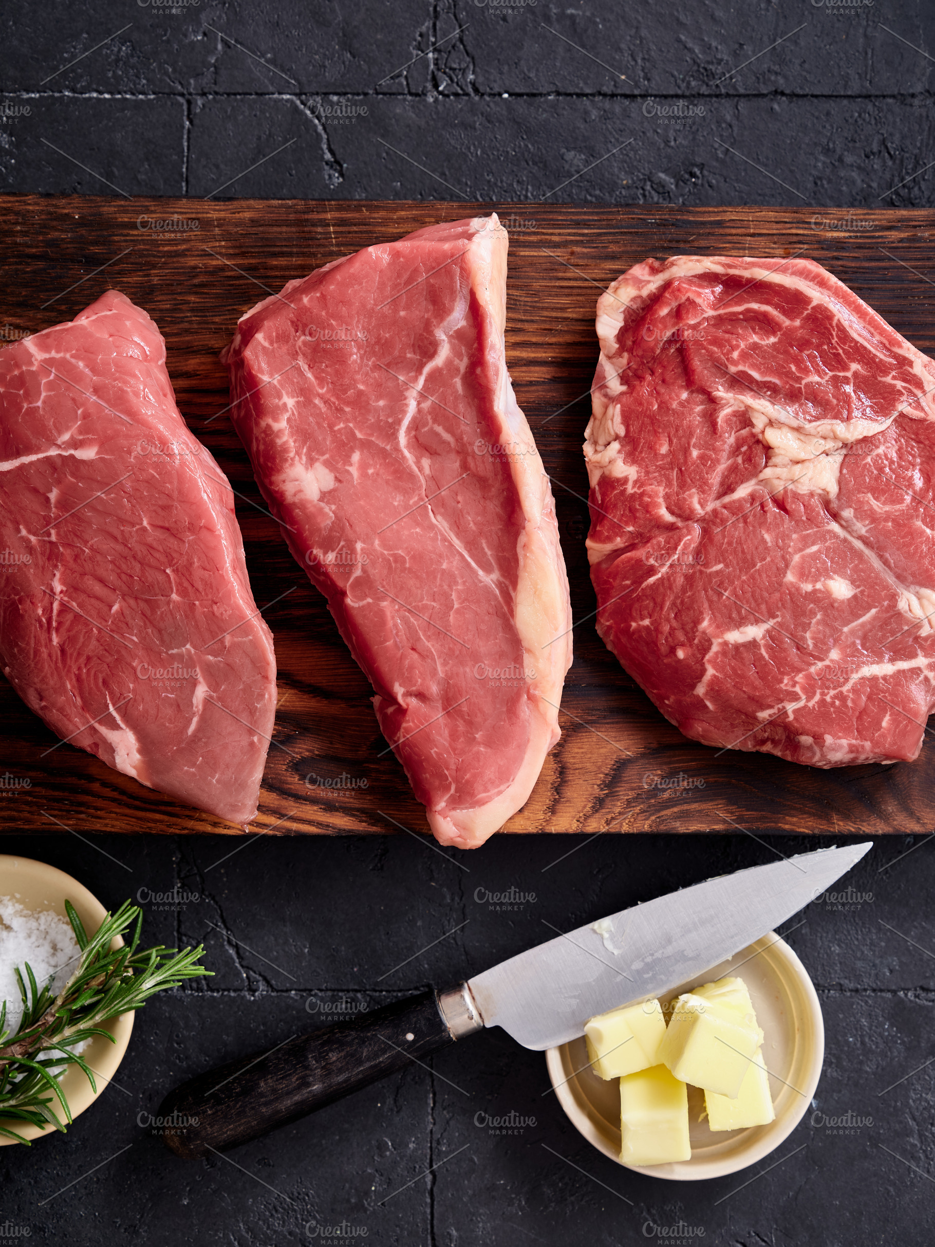 Different cuts of raw beef on a wooden board with butter, a knife, and herbs re, a Food & Drink Photo by Asya Nurullina
