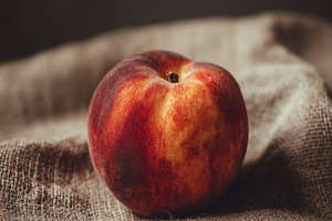 One peach on natural jute background, a Photo by Virgo Studio