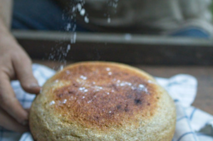 Baker's hand sprinkles flour on fresh bread close-up. A man finishes baking, de