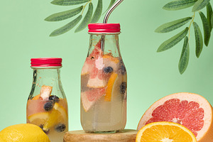 Glass bottles with lemonade and citrus fruit pieces on green bac, a Food & Drink Photo by ndanko