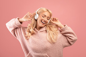 Playful lady enjoying playlist with closed eyes in wireless headphones, standin, a Photo by Prostock-Studio