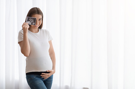 Happy Pregnant Woman With Ultrasound Scan Image Posing Near Window At Home, a Background Photo by Prostock-Studio