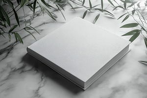 White book on marble with green leav, a Background Photo by Pixeness Studio