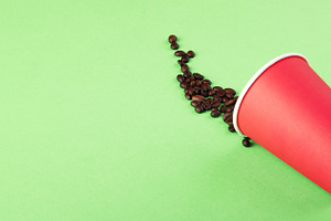 Coffee beans spilling from a red disposable cup on a vibrant gre, a Food & Drink Photo by Ales Munt