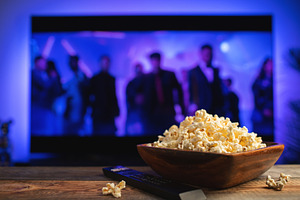 A wooden bowl of popcorn and remote control in the background the TV works, a Food & Drink Photo by Budarinphoto