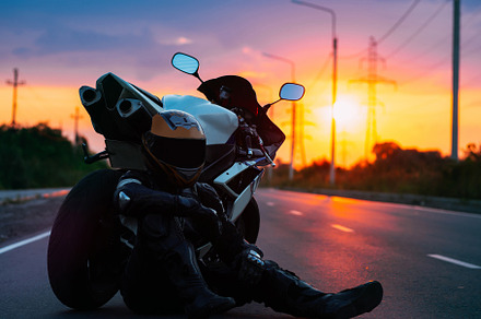 A motorcyclist in gear sits next to his motorcycle against the background of a, a Transportation Photo by PavelKant
