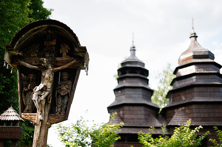 Wooden crucifix with historical church in the background under a cloudy sky, a Photo by AS photostudio