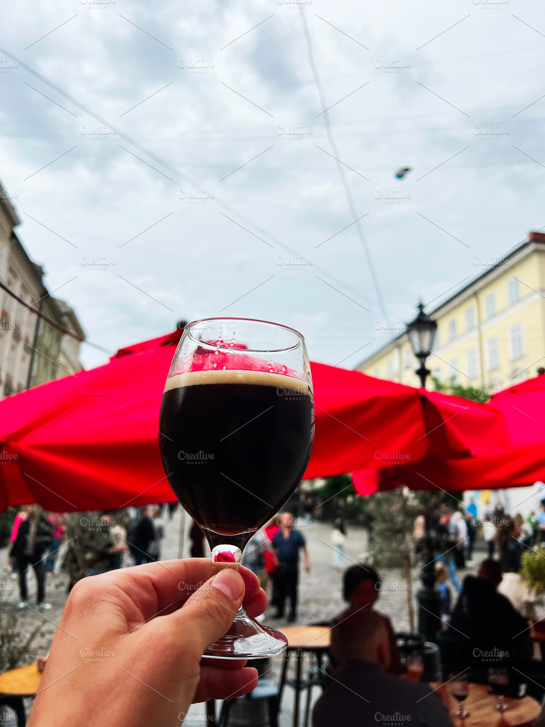 A hand holding a glass of dark beer in an outdoor setting, a Photo by AS photostudio