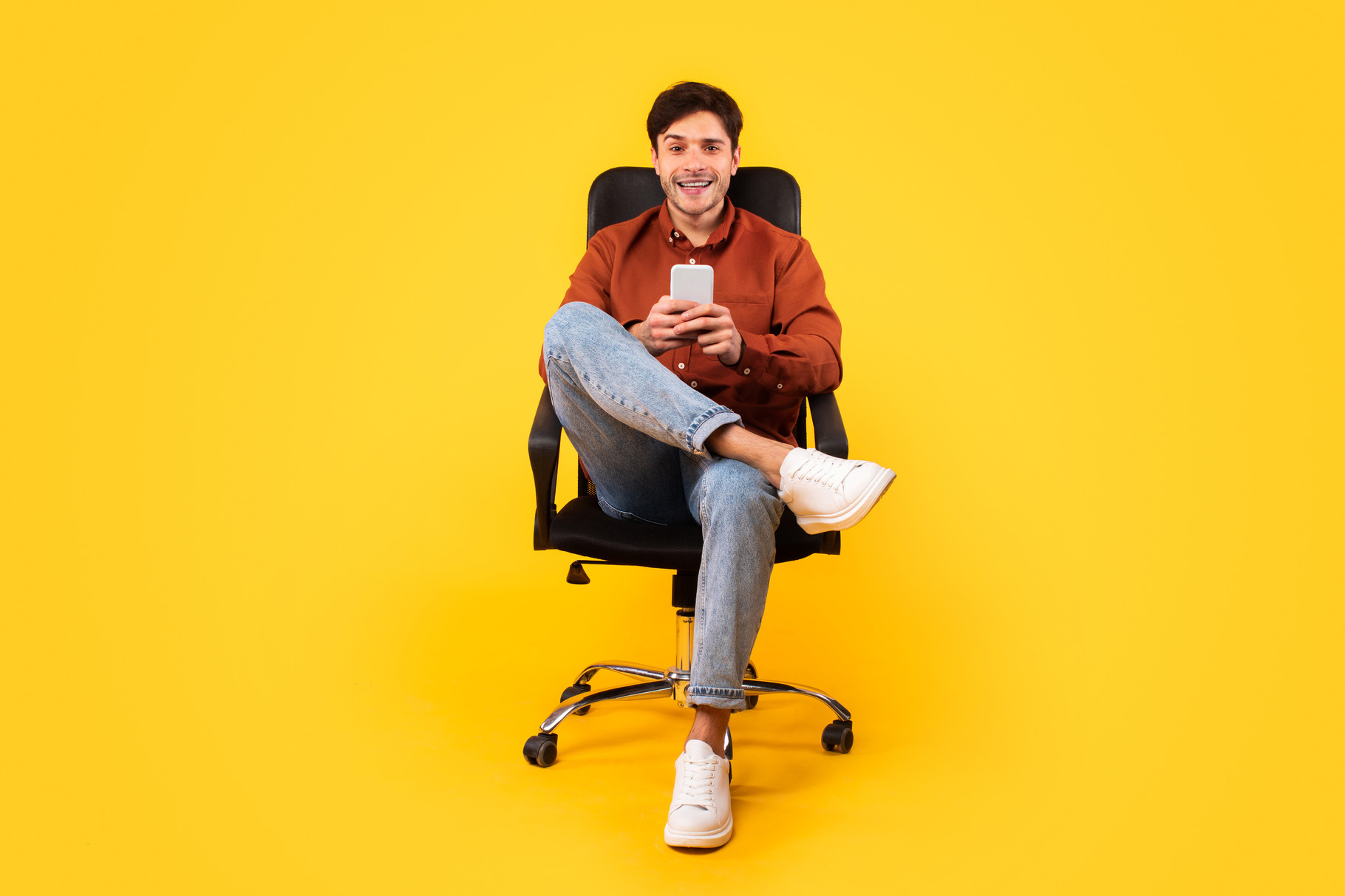 Happy Man Using Cellphone Sitting In Office Chair, Yellow Background, a ...