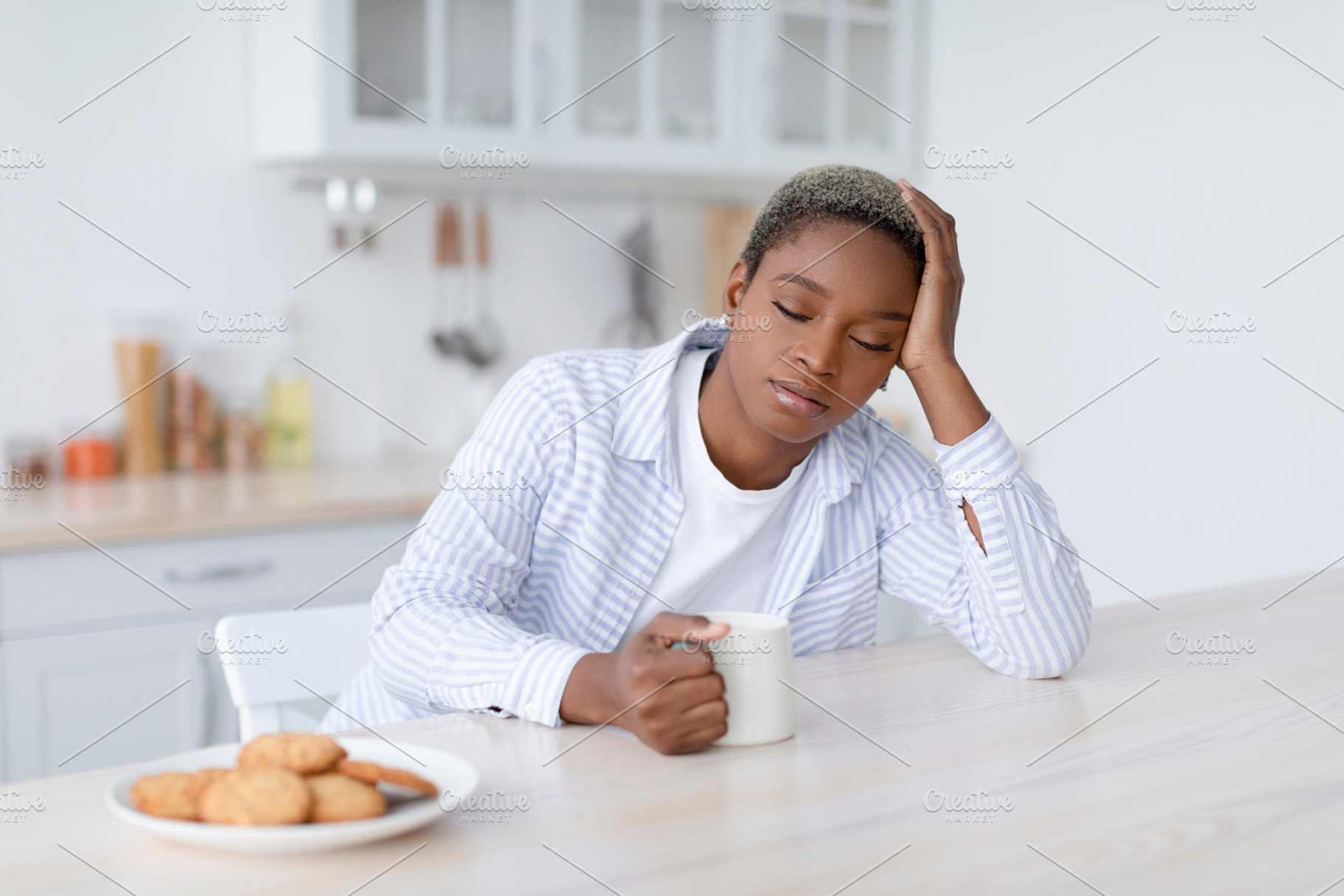 Tired sleepy young attractive black woman with cup of drink sits at table with, a Person Photo by Prostock-Studio