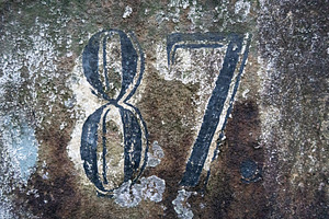 Faded number 87 painted on a weathered and mossy stone surface, an Architecture Photo by GoodGoods