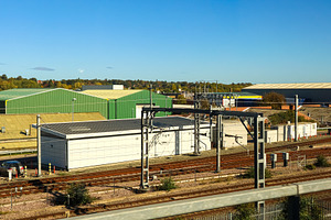 Railway tracks passing industrial warehouses under a sunny blue sky, urban tran, a Photo by Studio ANNA