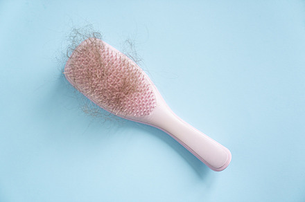 Hair loss concept - pink brush with lost hair on blue background