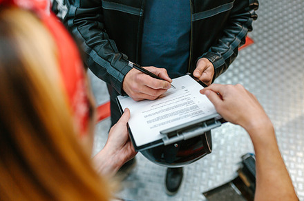 Female mechanic holding clipboard while biker man signing insurance policy on w, a Transportation Photo by davidpereiras