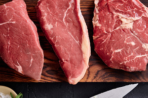 Different cuts of raw beef on a wooden board with butter, a knife, and herbs re, a Food & Drink Photo by Asya Nurullina