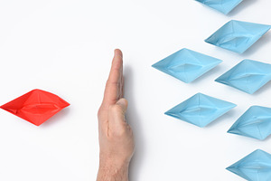 A hand stops a red paper boat while blue ones float past. The co, a Business Photo by ndanko