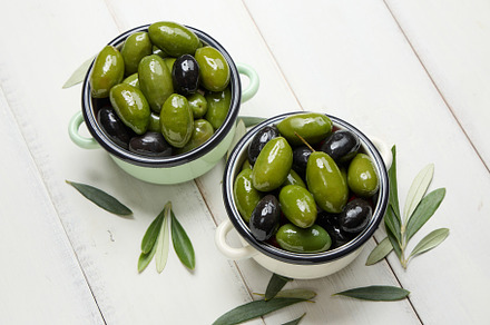 Green and black olives in small bowls on white planks background