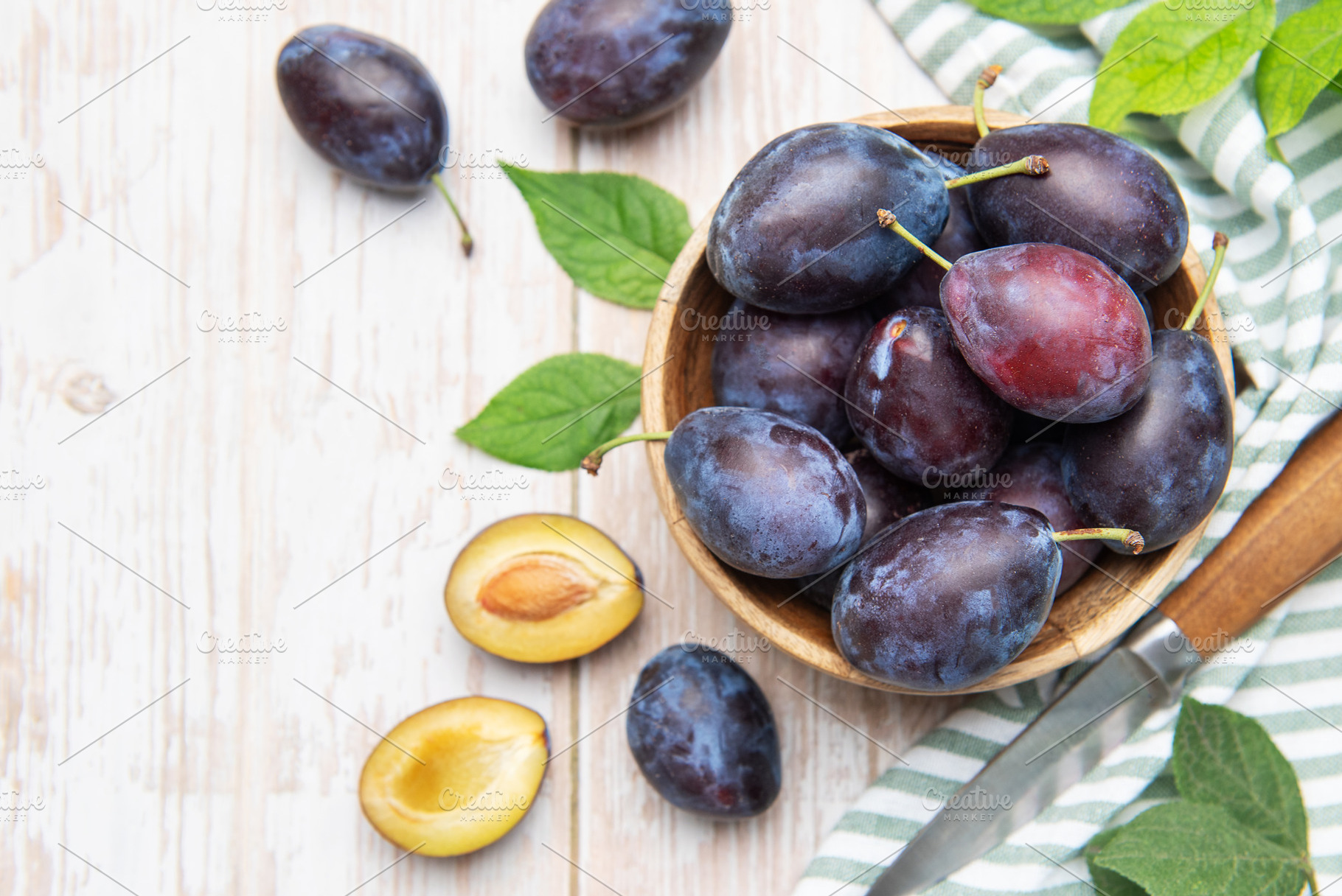 Fresh plums in wooden bowl with knife, a Food & Drink Photo by Olena Rudo
