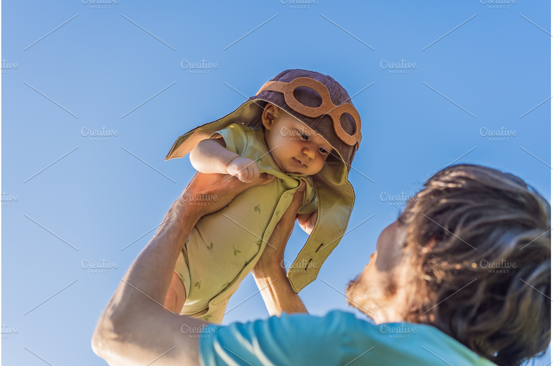 Father lifting baby in a pilot hat, a Person Photo by Elizaveta Galitskaya