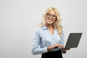 Happy young businesswoman using laptop computer against light grey studio backg, a Photo by Prostock-Studio