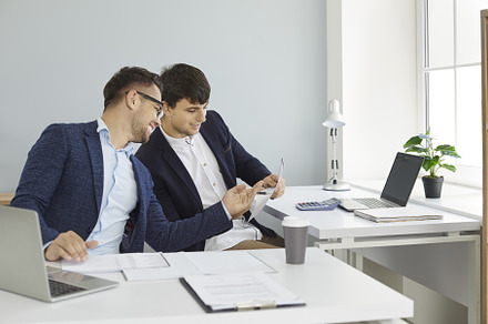 Two happy young men sitting at, a Business Photo by StudioRomantic