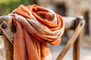 Hand-dyed silk scarf draped elegantly on rustic wooden railing under natural li, a Photo by AlyaAnd
