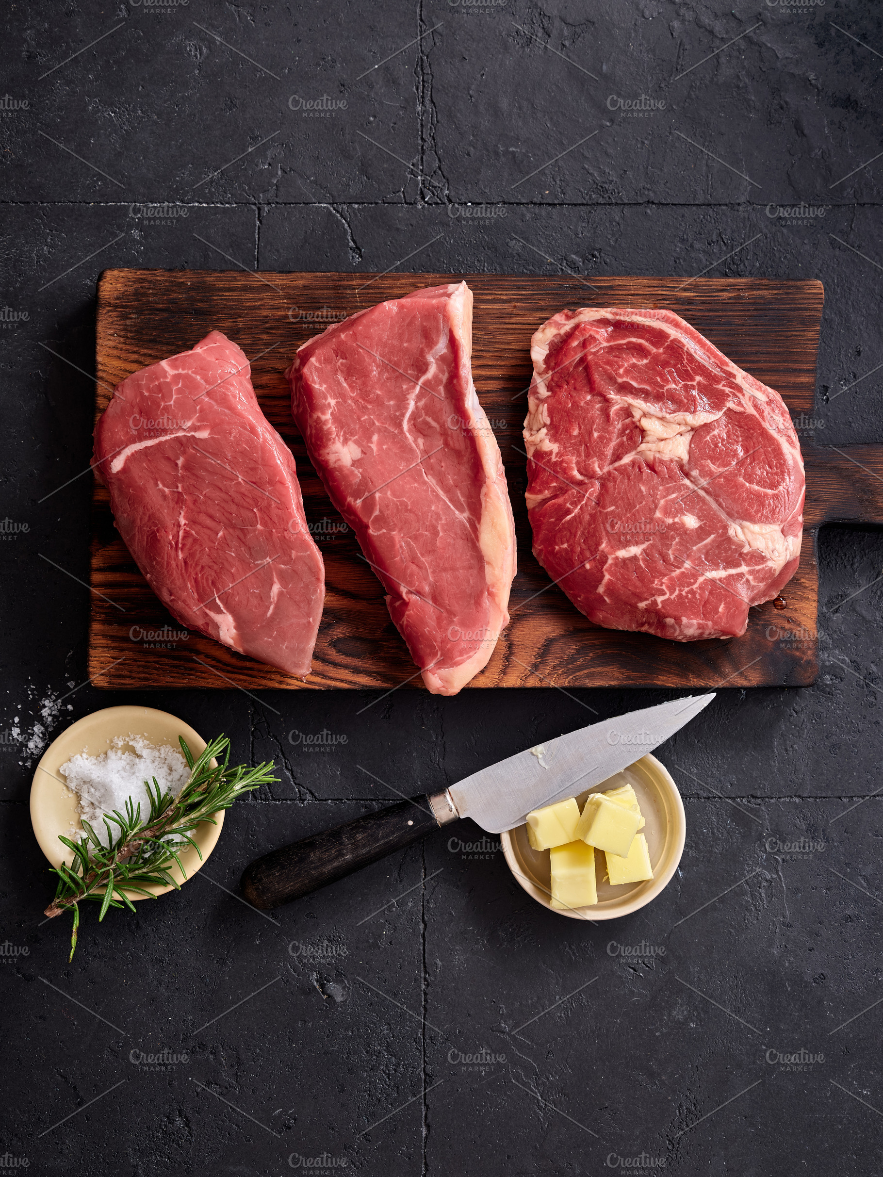 Raw rib-eye, roast beef, flank and rump steak arranged on a wooden cutting boar, a Food & Drink Photo by Asya Nurullina